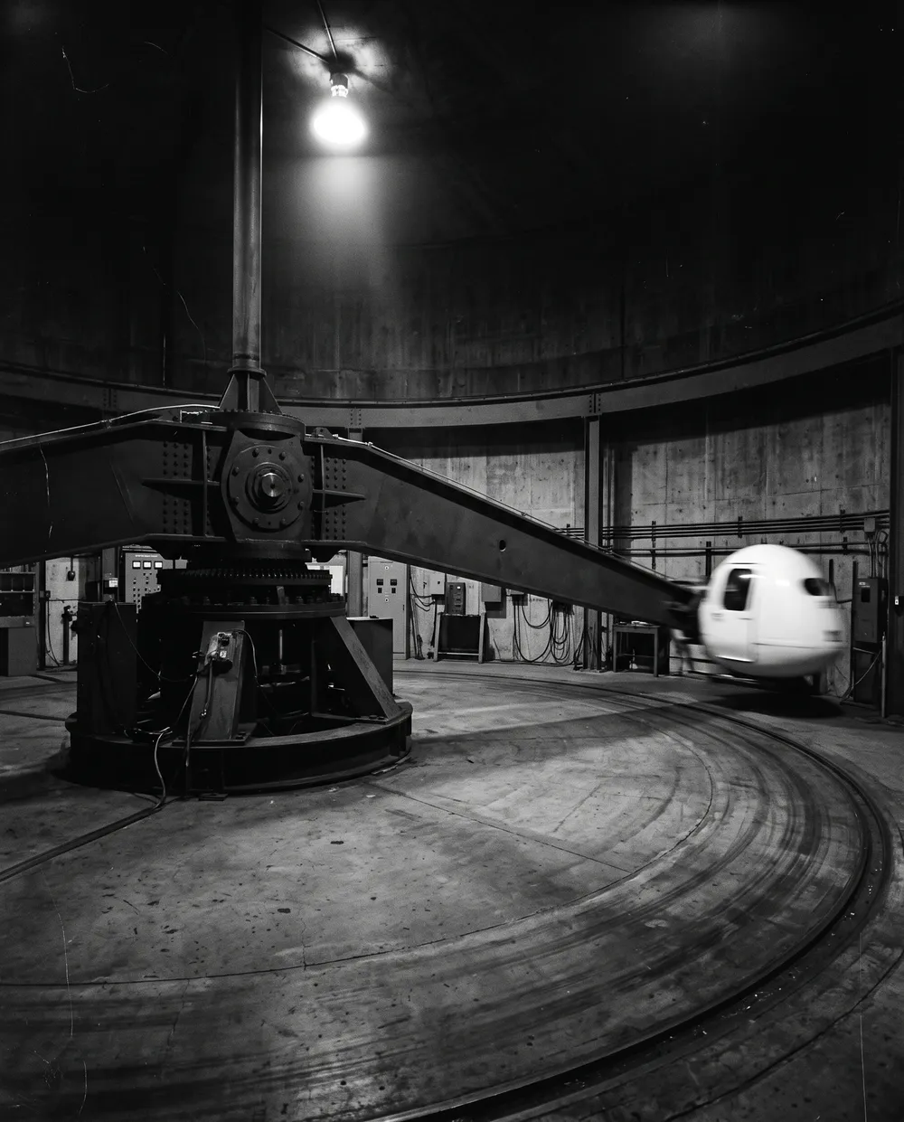 A human centrifuge: a long steel arm with a capsule sweeping around a circular concrete hall